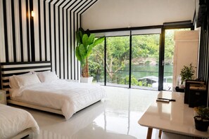 Un dormitorio moderno con una cama grande, un escritorio y vistas a un lago a través de ventanas de pared a techo.