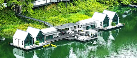 A floating house with a dock, surrounded by lush greenery and water.