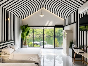 A modern bedroom with a large bed, a desk, and a view of a lake.