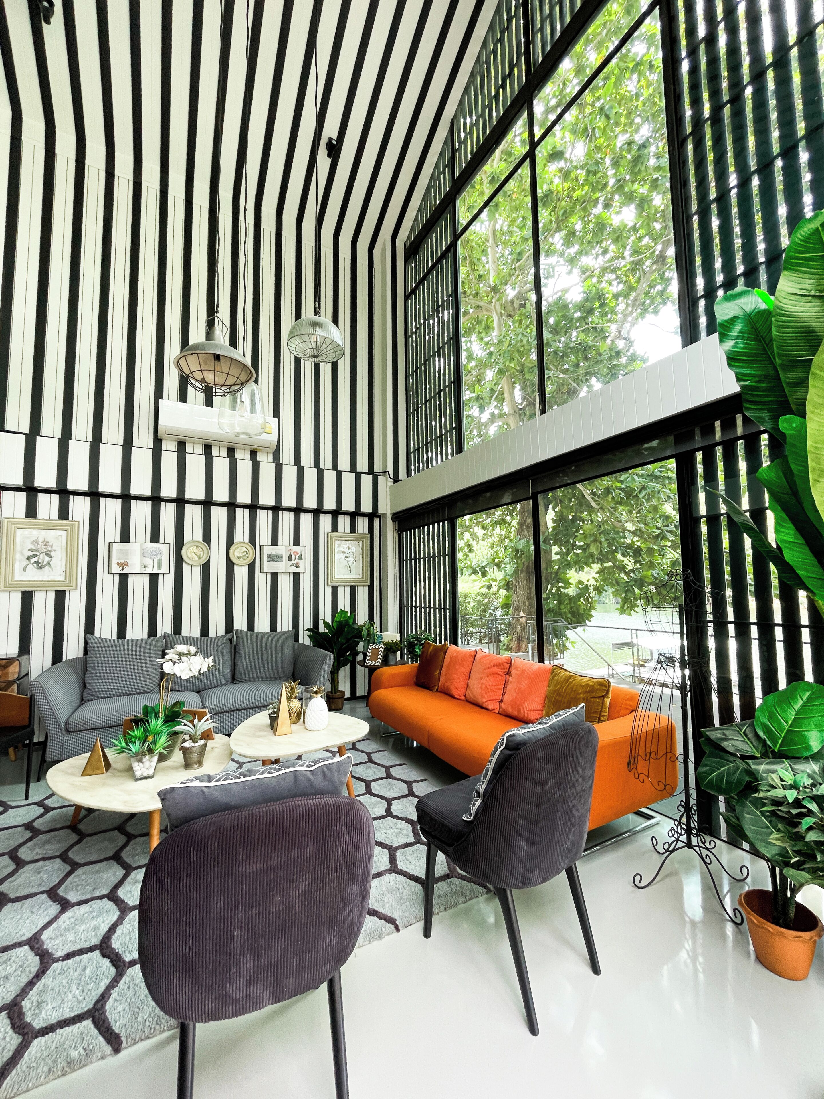 Un salon moderne avec un mur à rayures, un canapé, une table basse et une vue dégagée sur l’extérieur grâce à de grandes fenêtres.