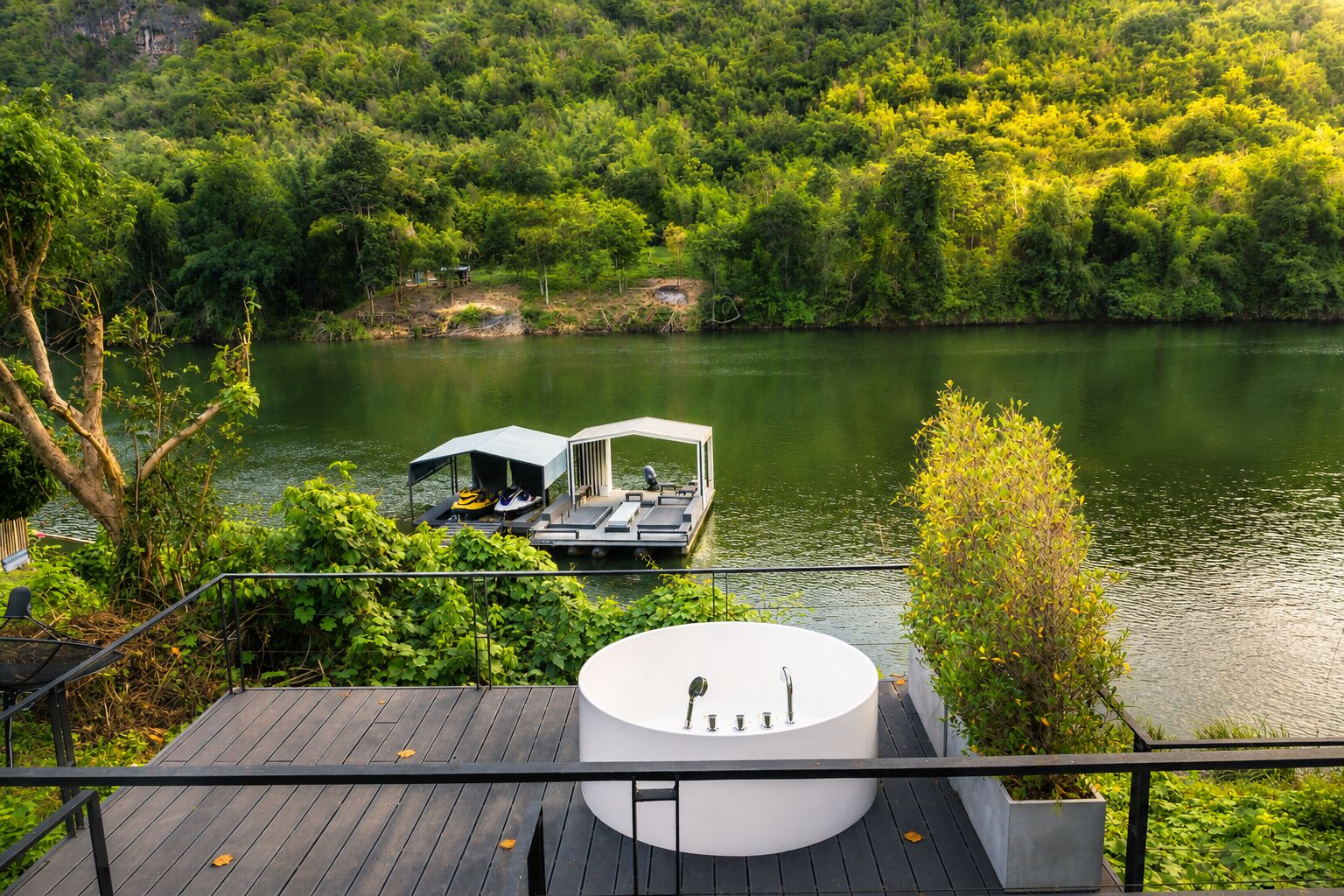 Une terrasse au bord du lac avec un jacuzzi, un abri pour bateaux et une végétation luxuriante.