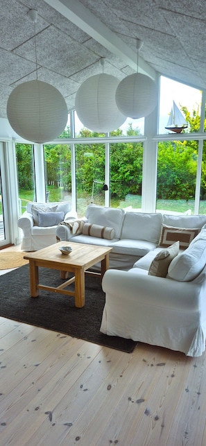 Una sala de estar moderna con un sofá blanco, una mesa de centro de madera y ventanas amplias con vistas al exterior.
