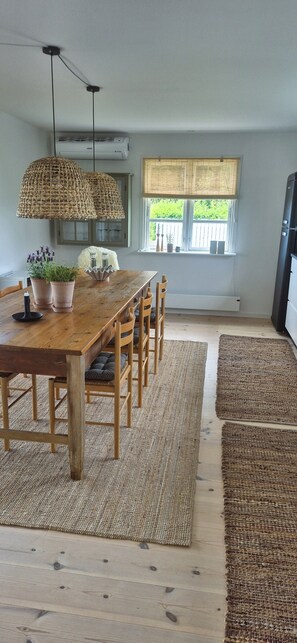 A dining area with a wooden table and chairs, a hanging light fixture, and a window with a view of greenery.