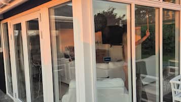 A covered outdoor area with sliding glass doors, a wooden deck, and a seating area with a table and chairs.