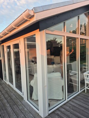 A covered outdoor area with sliding glass doors, a wooden deck, and a seating area with a table and chairs.