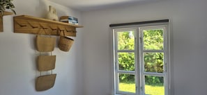 A room with a wooden shelf holding books and a vase, a set of woven baskets, and a double door window with a view of greenery.