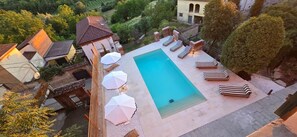 A swimming pool with lounge chairs and umbrellas, surrounded by trees and buildings.
