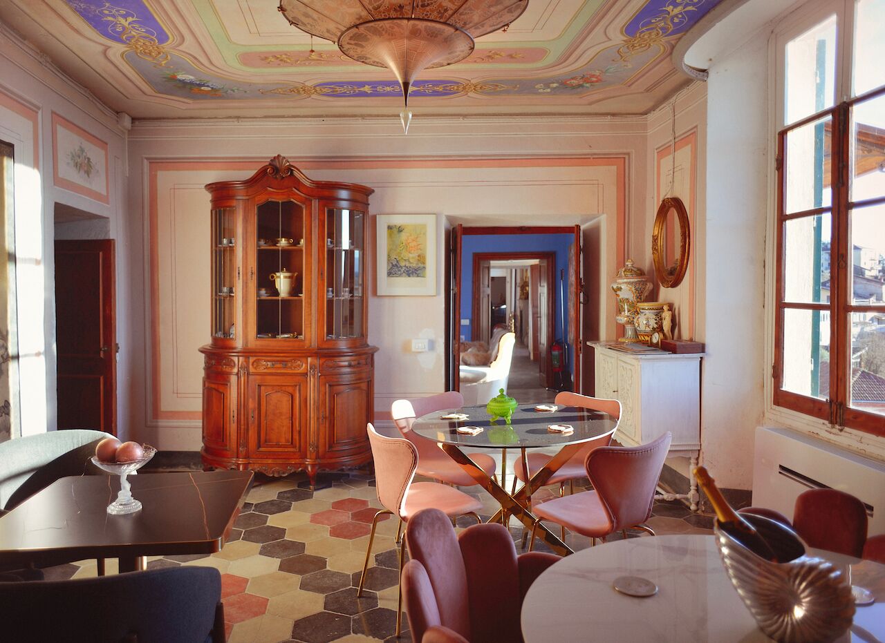 A dining area with a round table, chairs, a cabinet with glass doors, and a view through an open door.