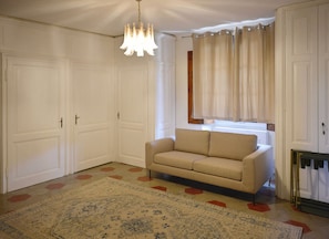 A room with a beige sofa, a patterned rug, and a chandelier.