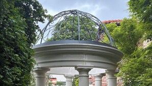 A gazebo with a metal roof and white columns, surrounded by greenery and a brick wall. - Club Carpeneto  (Carpeneto)