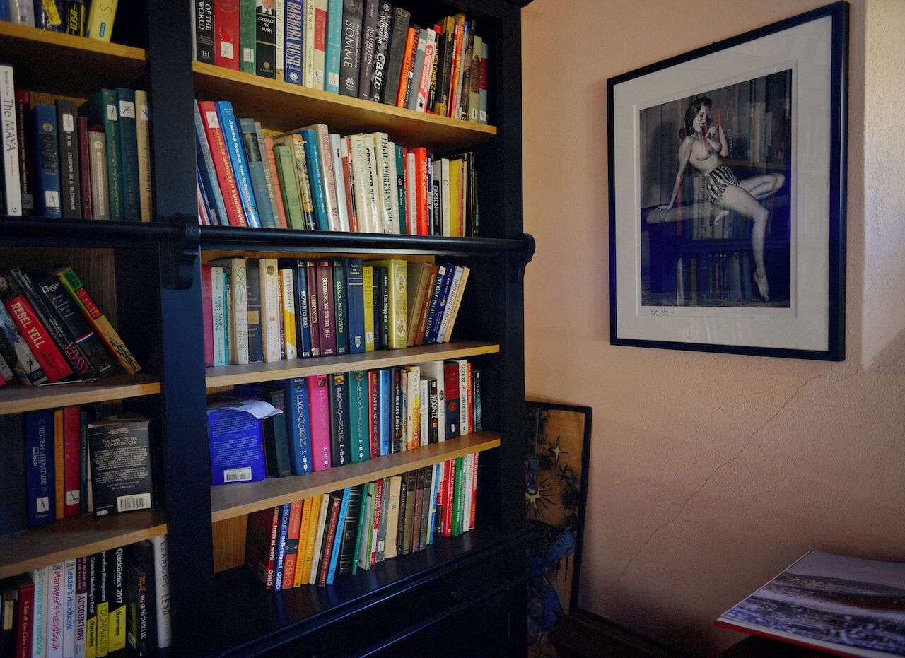 Une bibliothèque remplie de livres, une œuvre d’art encadrée accrochée au mur et une petite table sur laquelle repose un livre.