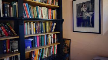 Une bibliothèque remplie de livres, une œuvre d’art encadrée accrochée au mur et une petite table sur laquelle repose un livre.