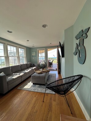 A living room with a sectional sofa, a coffee table, a black chair, and a view of the outdoors through large windows.