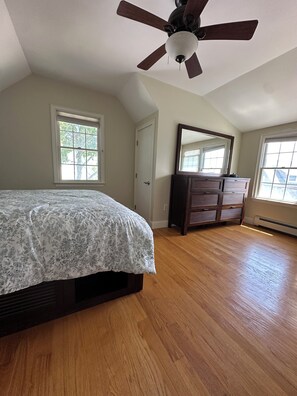 A bedroom with a bed, a dresser, a ceiling fan, and two windows.