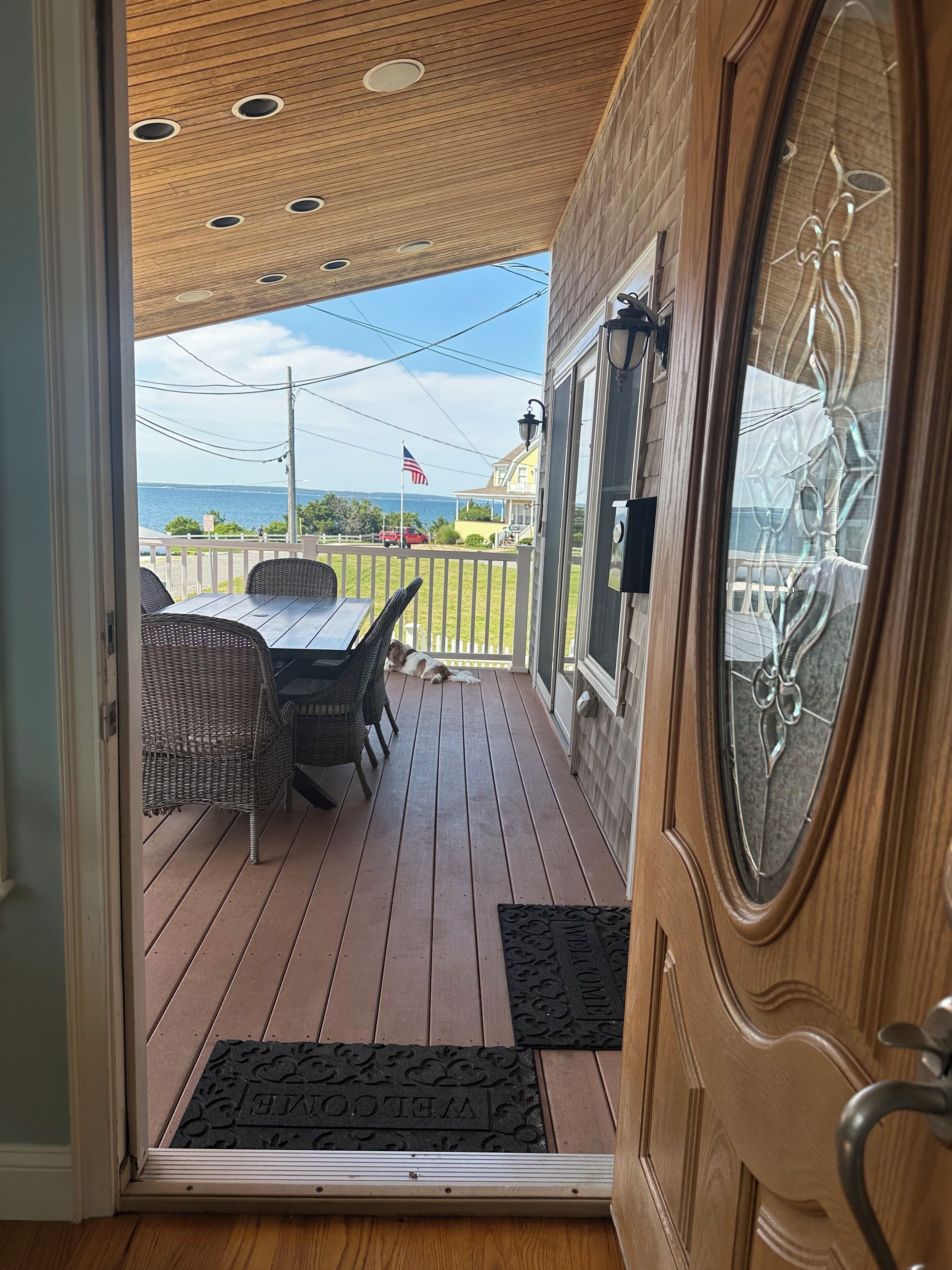 A wooden deck with a view of the sea, a covered patio area, and a door with a glass panel.