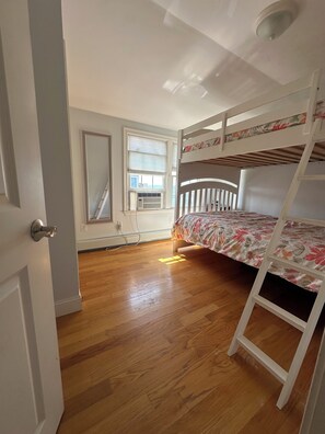 Une chambre avec un lit superposé, un plancher en bois, un radiateur et une fenêtre avec des stores.