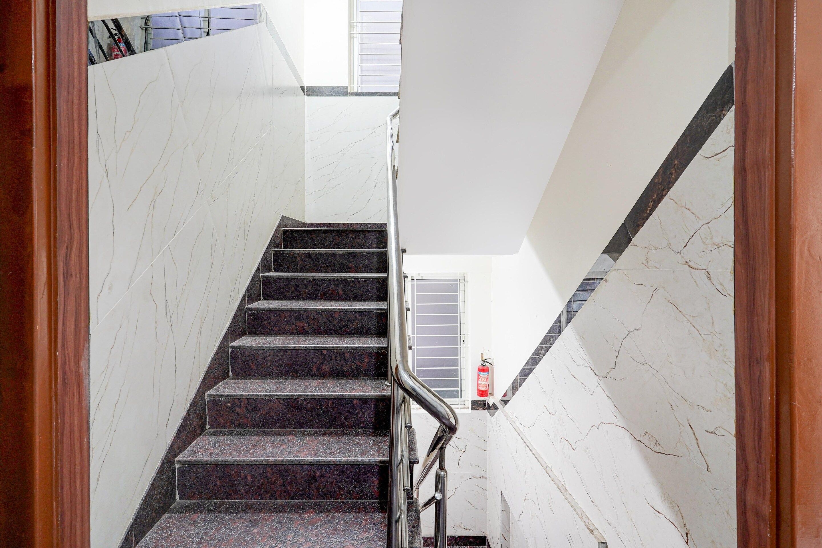 A staircase with marble walls and a fire extinguisher on the landing.