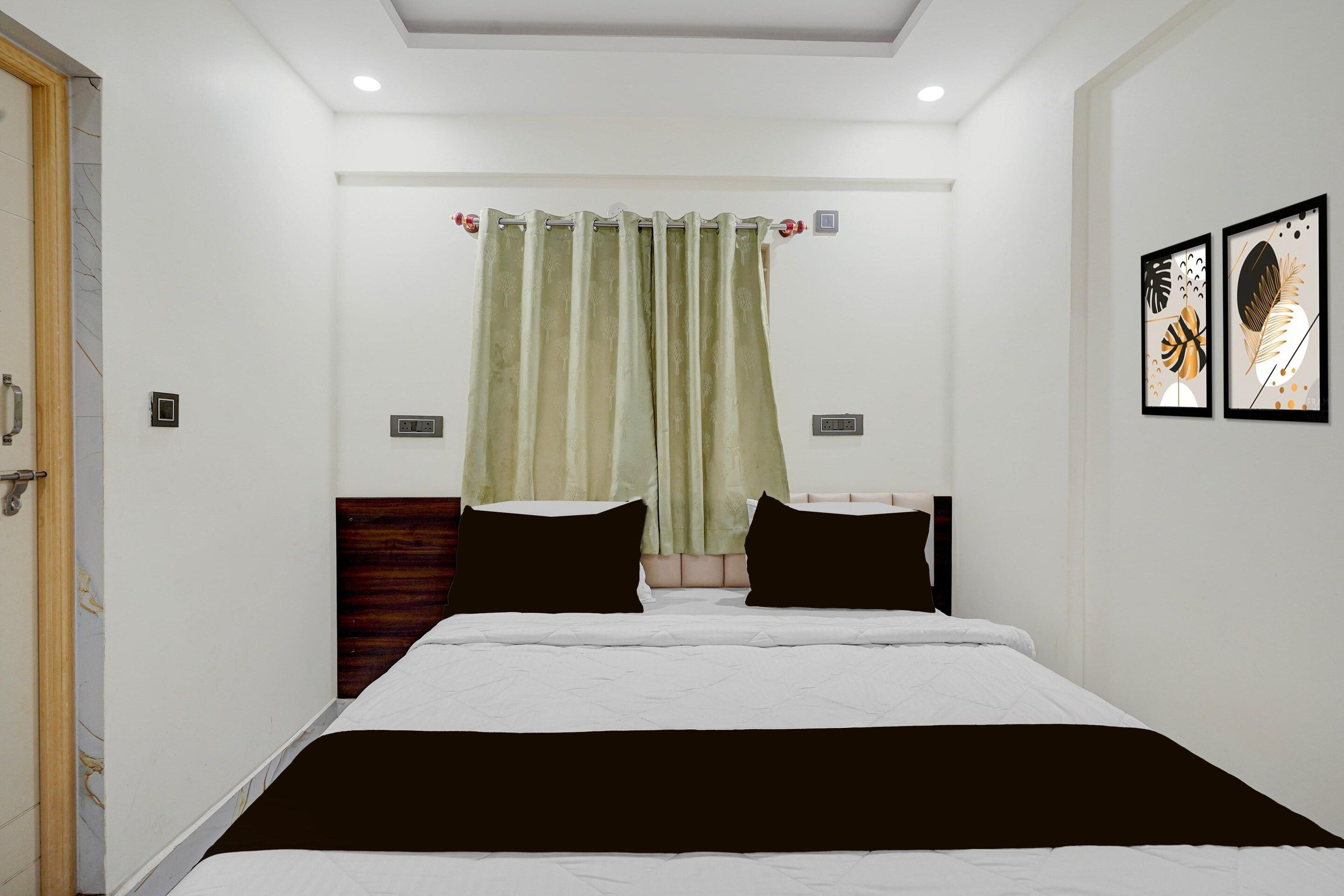 A bedroom with a bed, two bedside tables, a window with curtains, and two wall-mounted artworks.