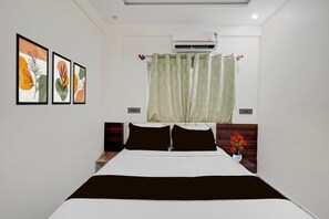 A hotel room with a bed, a nightstand, a wall-mounted air conditioner, and a window with a curtain. - Townhouse Chinnappanahalli (Bengaluru)