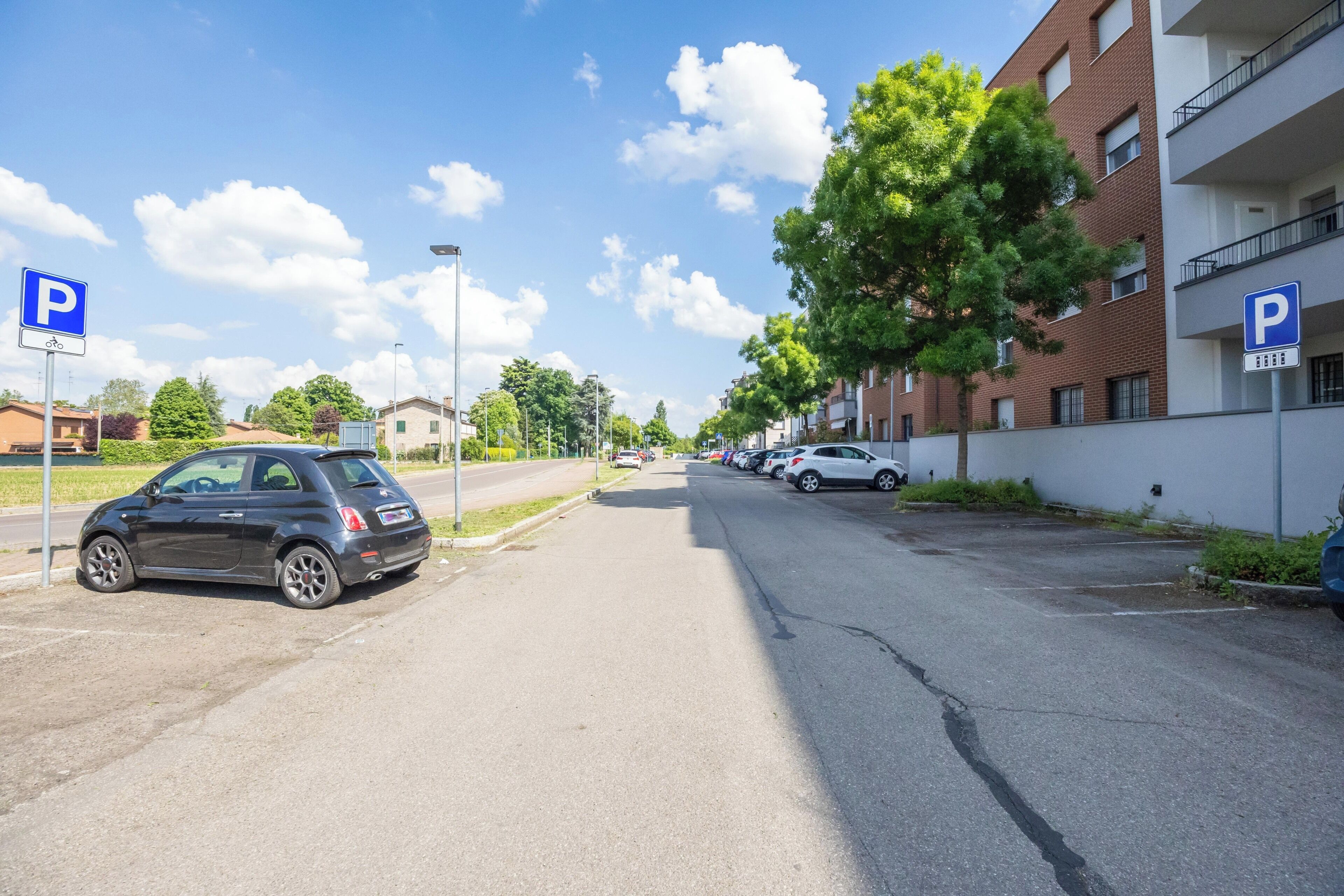 Calle con coches estacionados y un edificio con un letrero de estacionamiento.