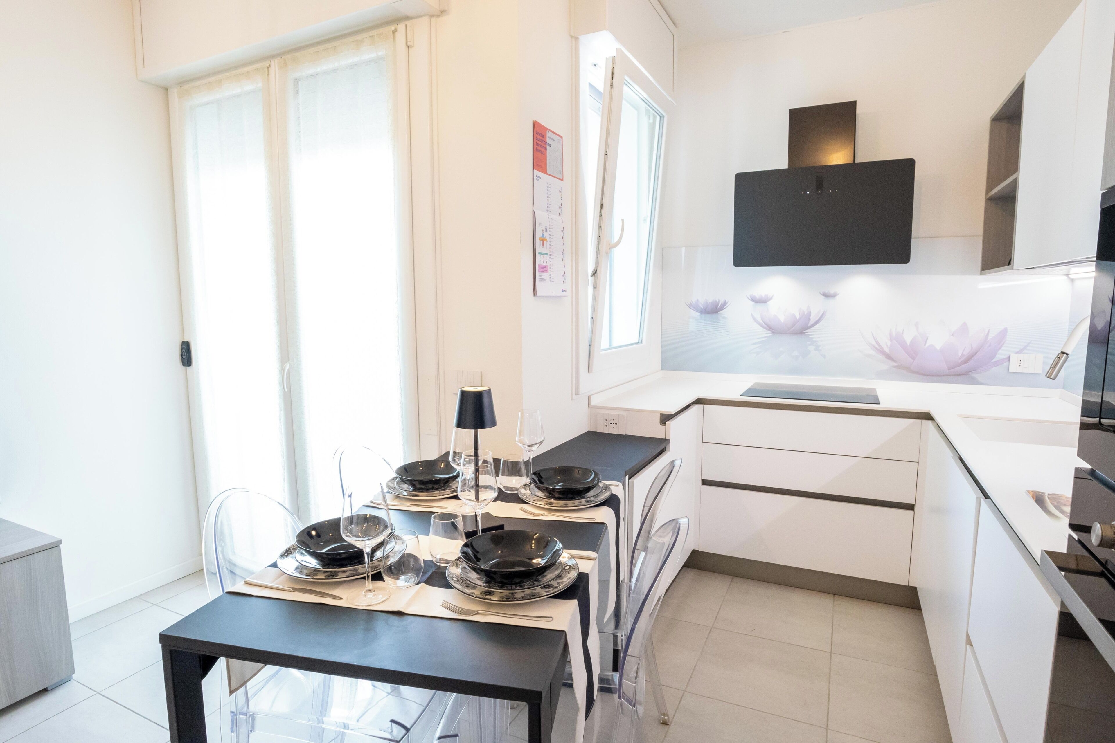 A modern kitchen with white cabinetry, a dining table set with plates and glasses, and a window with a view of lotus flowers.