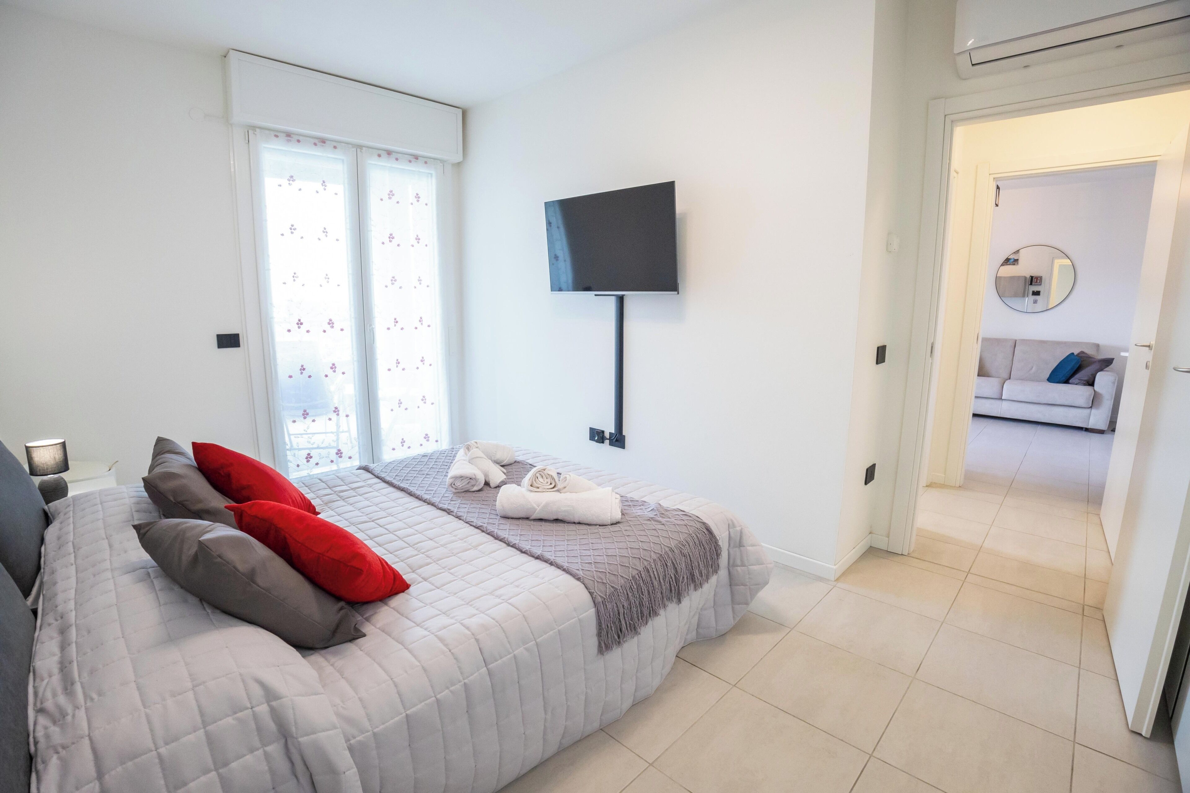 A bedroom with a bed, pillows, a TV, and a view into another room.