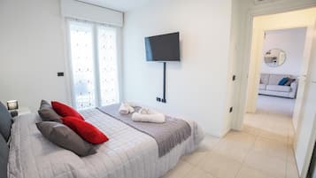 A bedroom with a bed, pillows, a TV, and a view into another room.