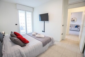 A bedroom with a bed, pillows, a TV, and a view into another room. - Le Ninfee • Tourist Apartment (Zola Predosa)