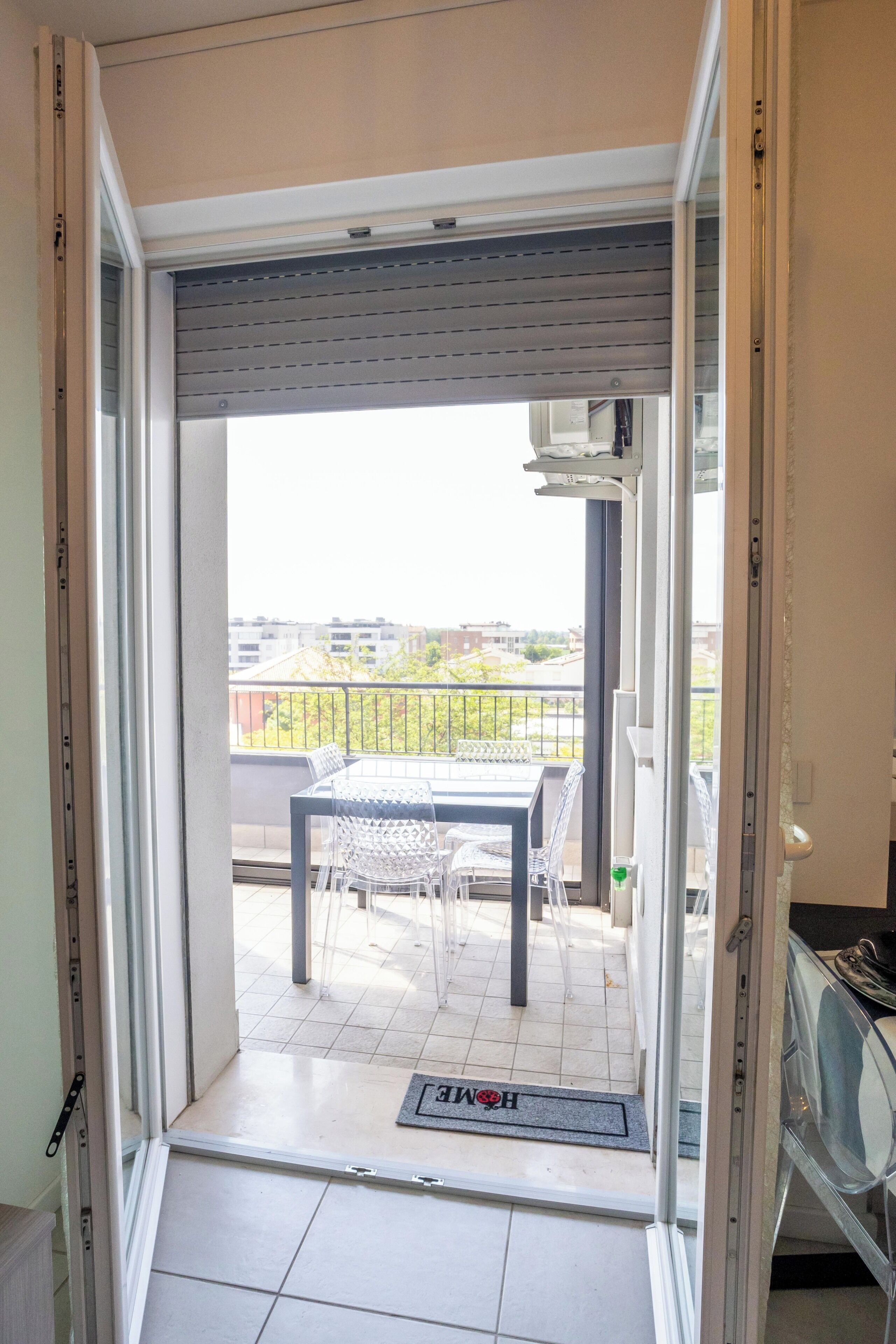 Un balcón con mesa y sillas, un felpudo y vistas a edificios distantes.