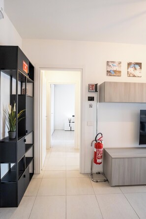 A modern interior with a black bookshelf, a fire extinguisher, and a hallway leading to another room.