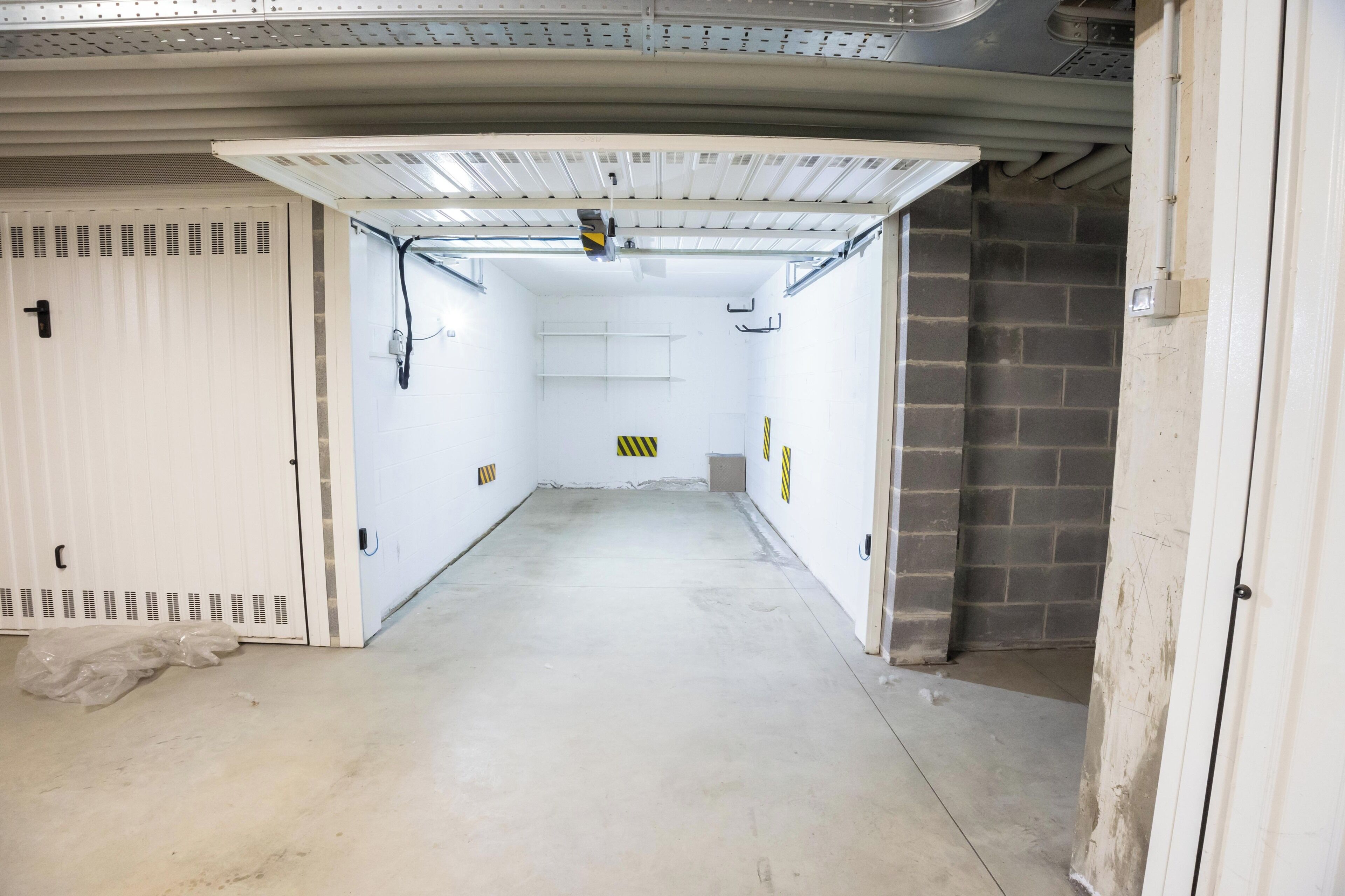 A clean, empty hallway with a white door on the left, a brick wall on the right, and a ceiling with ventilation ducts.