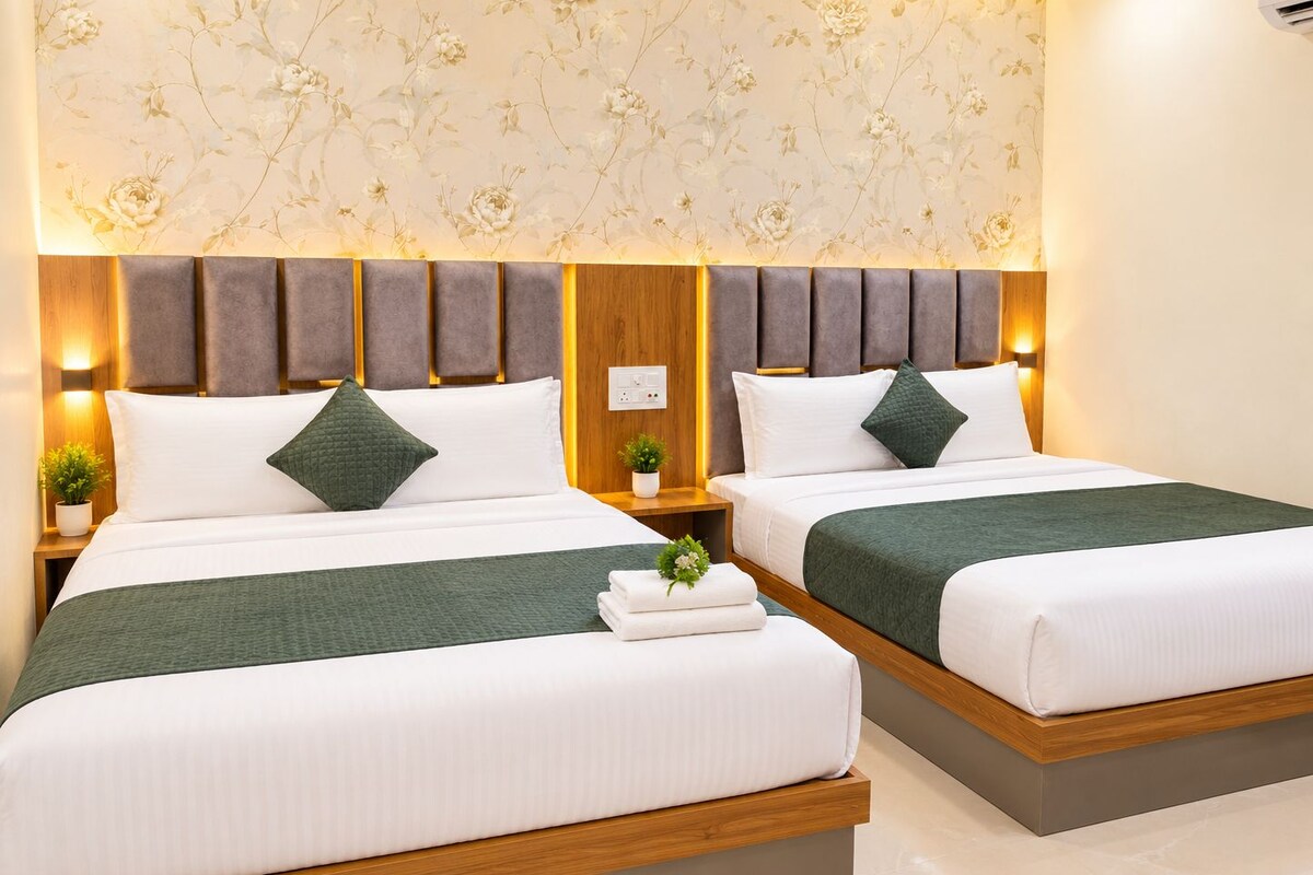 A hotel room with two beds, each with a wooden headboard, white bedding, and green throw pillows.