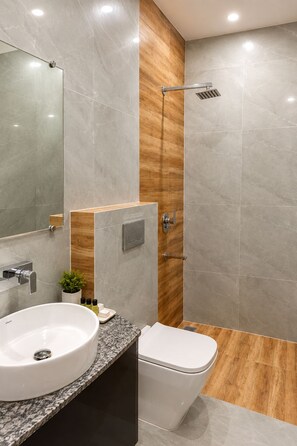 A modern bathroom with a marble vanity, a toilet, and a shower with a wooden accent wall. - Hotel Grey Stone B & B (Amritsar)