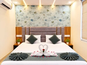 A hotel room with a large bed, floral wallpaper, a headboard, bedside tables with lamps, and a decorative swan on the bed. - Hotel Grey Stone B & B (Amritsar)