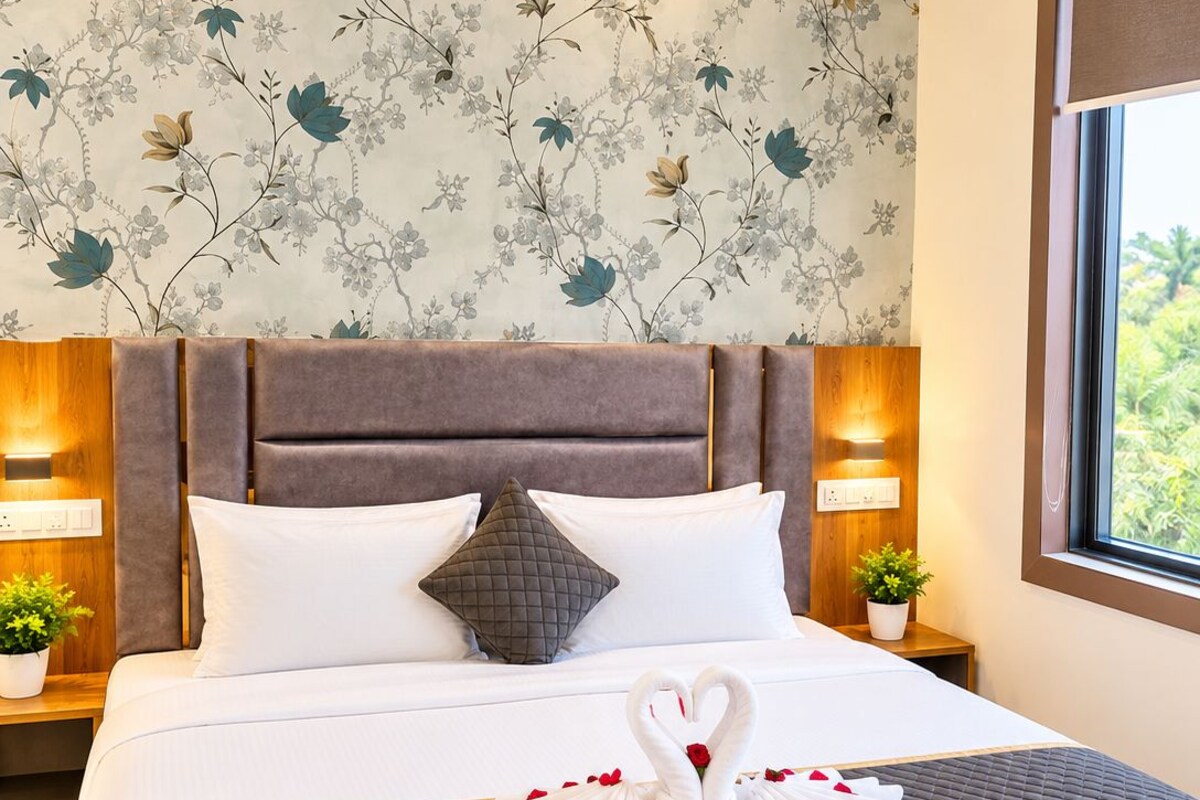A neatly made bed with a quilted bedspread, two pillows, and a decorative swan towel arrangement.