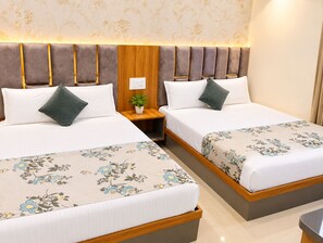A hotel room with two beds, each with a floral bedspread, a nightstand with a plant, and a wooden headboard. - Hotel Grey Stone B & B (Amritsar)