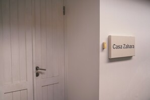 Eine weiße Tür mit einem Metallgriff und Schlüsselloch, und ein Schild an der Wand mit der Aufschrift 'Casa Zahara'.