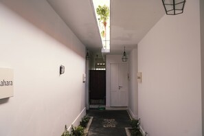Ein schmaler Flur mit einer Tür am Ende, einer kleinen Pflanze und einem Schild an der Wand.
