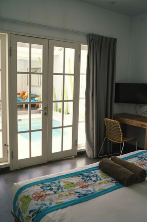 Ein Hotelzimmer mit Bett, Schreibtisch, Stuhl, Fernseher und einer Glasschiebetür, die zu einem Poolbereich führt.