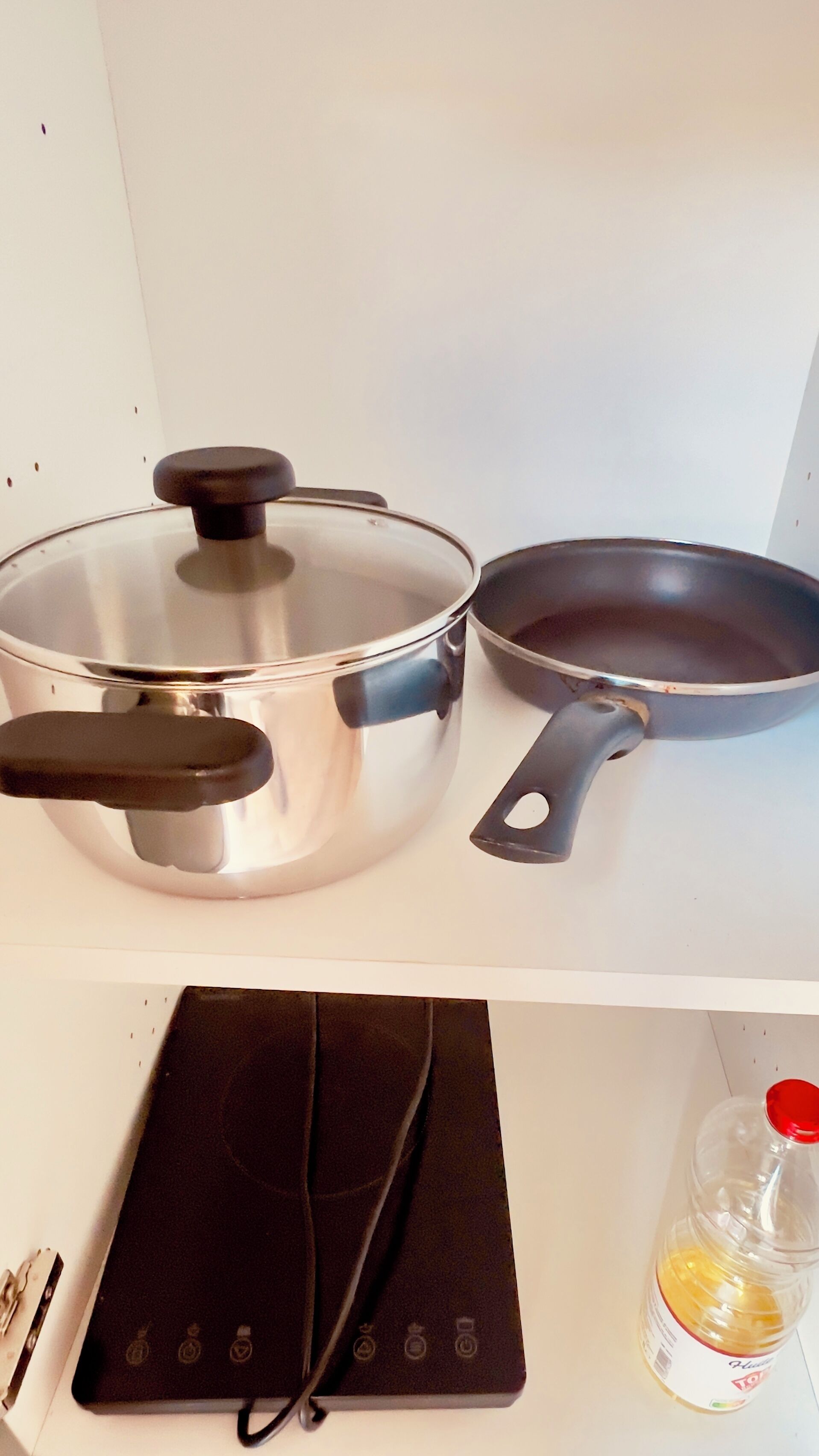 A kitchen with a stainless steel pot, a frying pan, a black electric kettle, and a bottle of honey.
