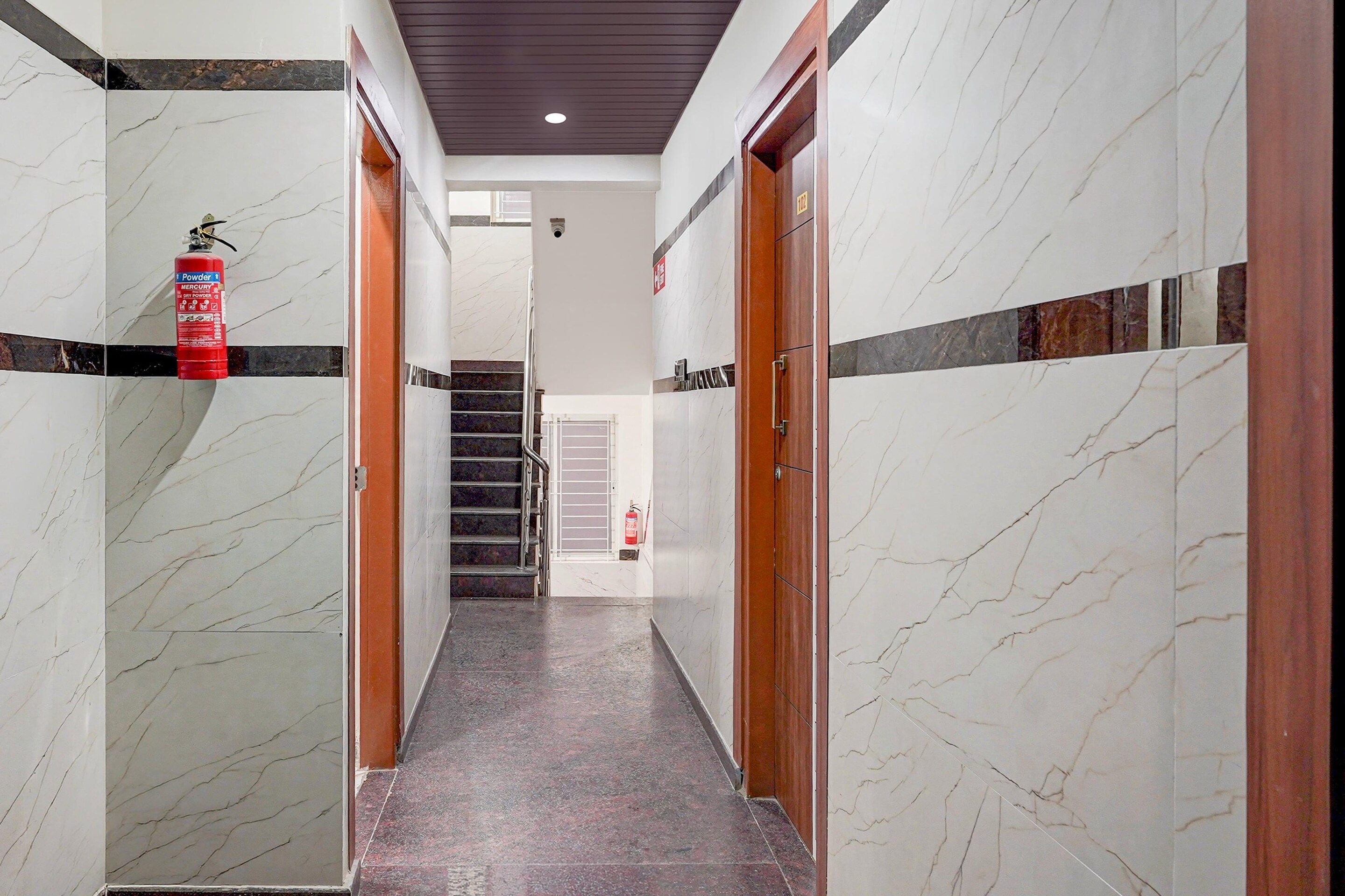 A hallway with marble walls, wooden doors, and a fire extinguisher mounted on the wall.