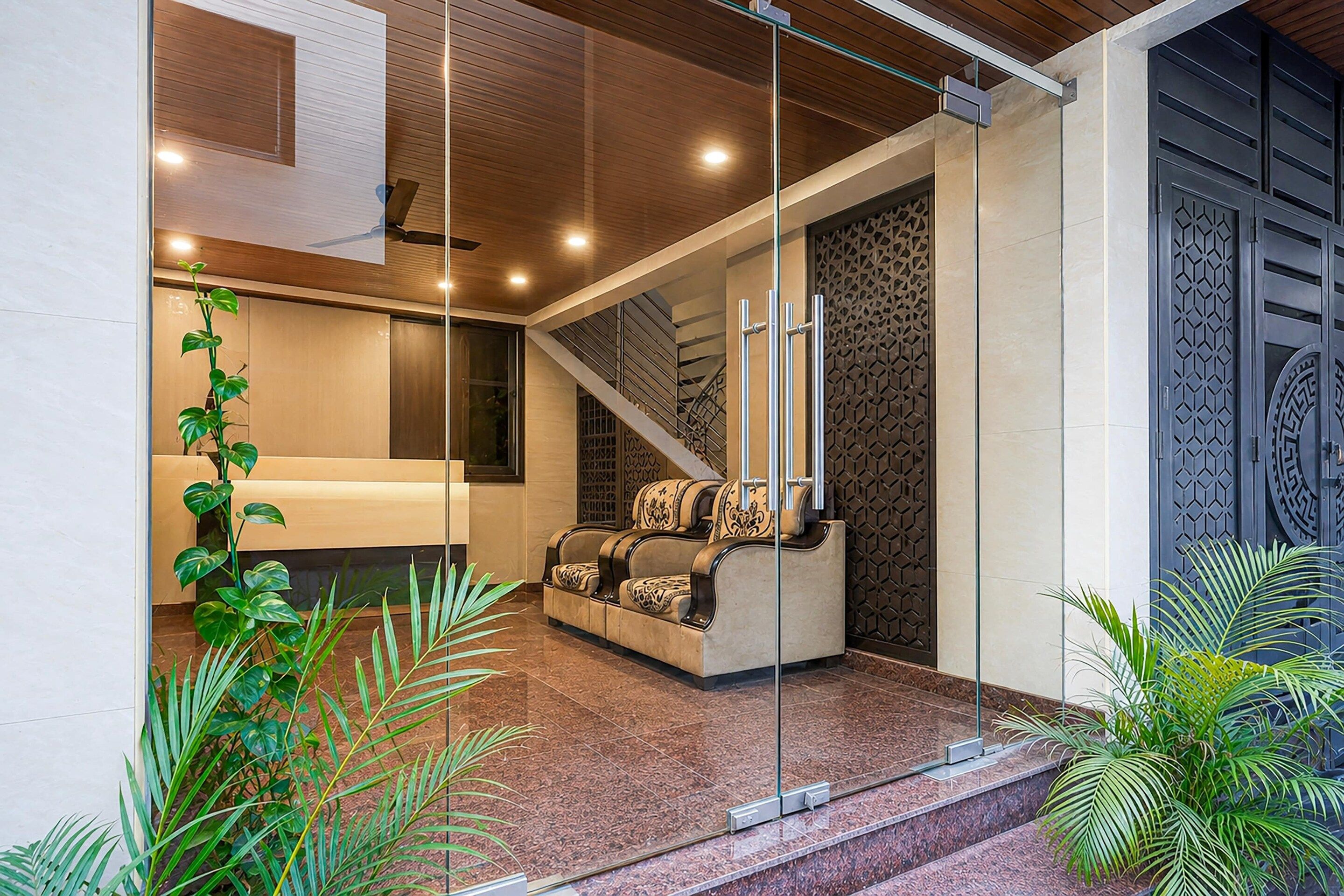 Un interior modern amb un separador de vidre, un sofà, una escala i panells decoratius.