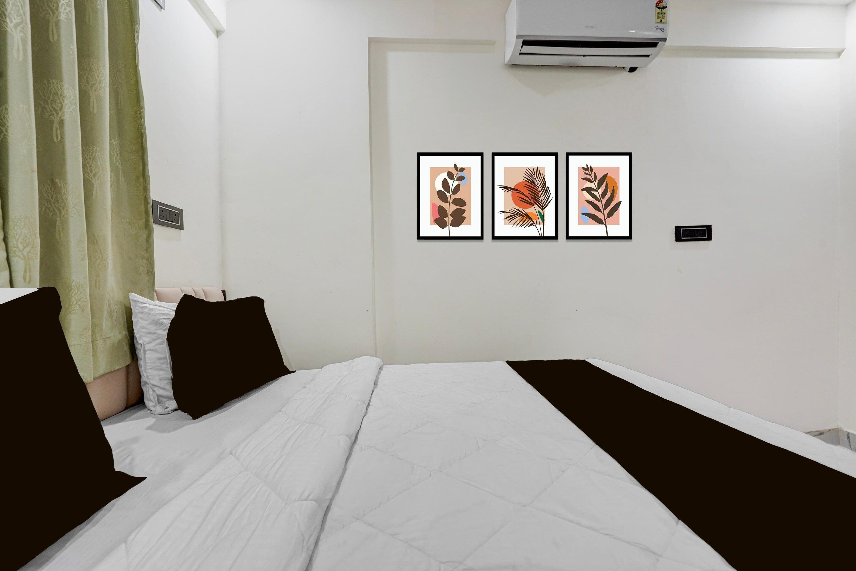A hotel room with a bed, a wall-mounted air conditioner, and three framed artworks.