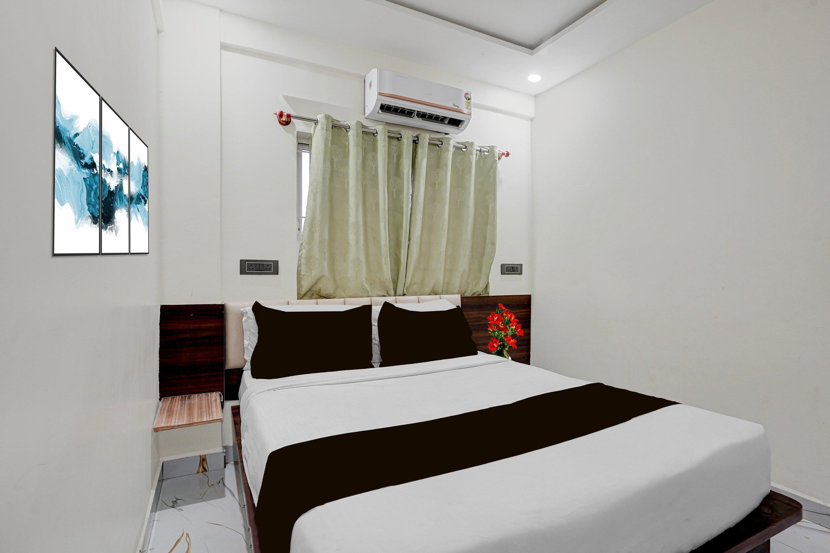 A hotel room with a bed, a window with curtains, an air conditioning unit, and a wall-mounted artwork.