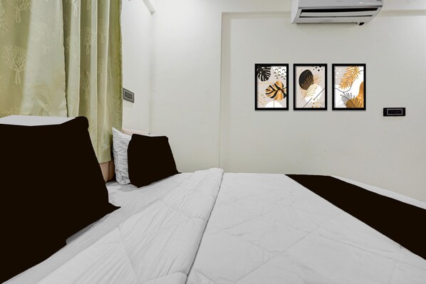 A hotel room with a bed, a wall-mounted air conditioner, and three framed artworks.