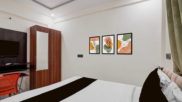 Ein Hotelzimmer mit einem Bett, einem Schreibtisch mit Computer, einem Fernseher und drei gerahmten Kunstwerken an der Wand.