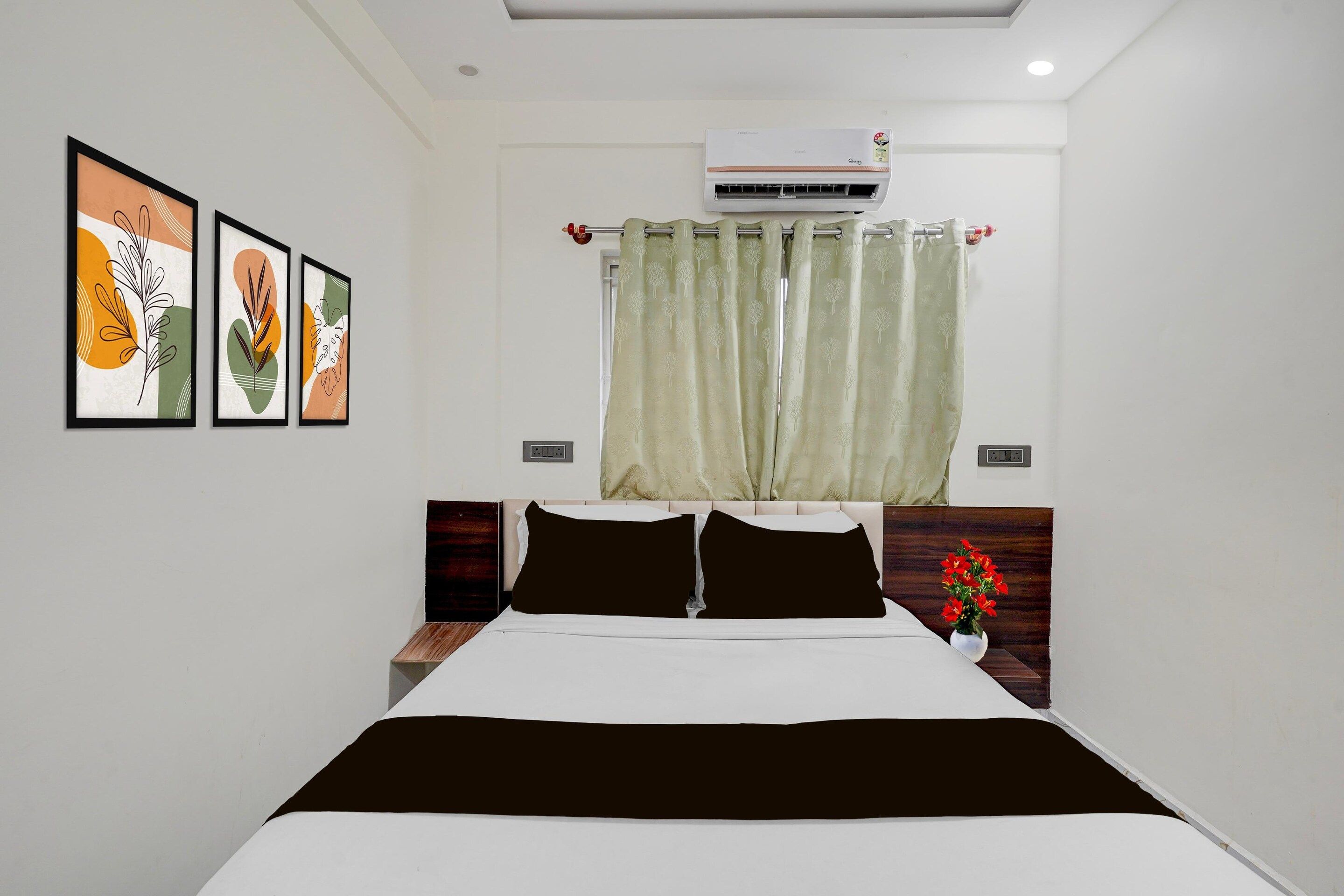 A hotel room with a bed, a nightstand, a wall-mounted air conditioner, and a window with a curtain.