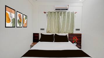 A hotel room with a bed, a nightstand, a wall-mounted air conditioner, and a window with a curtain.