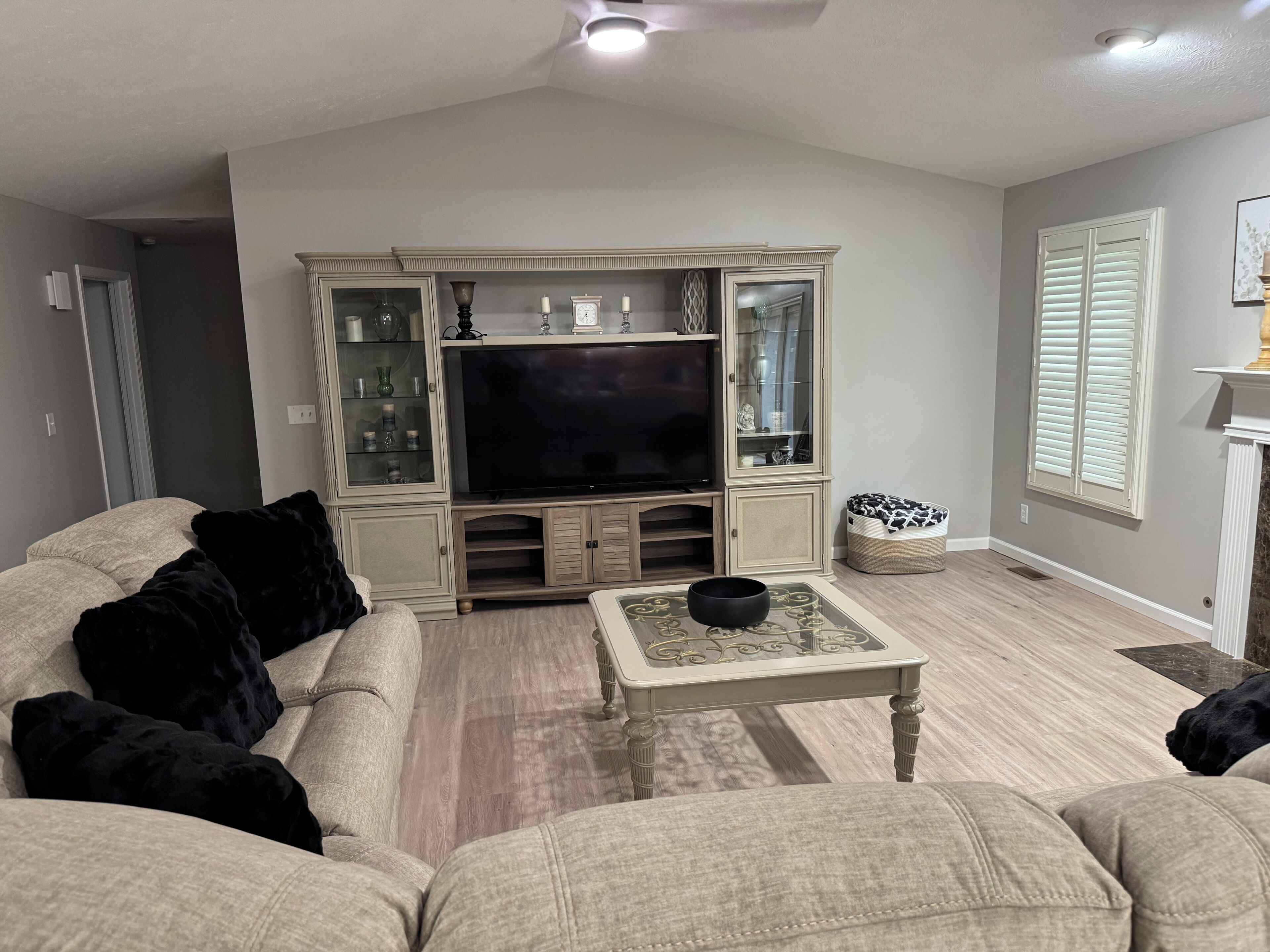Una sala de estar con una televisión, un mueble con puertas de cristal, una mesa de centro y una cama para perro.