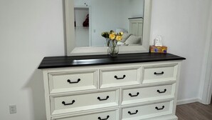 A white dresser with black handles and a black top, placed against a white wall with a mirror above it.